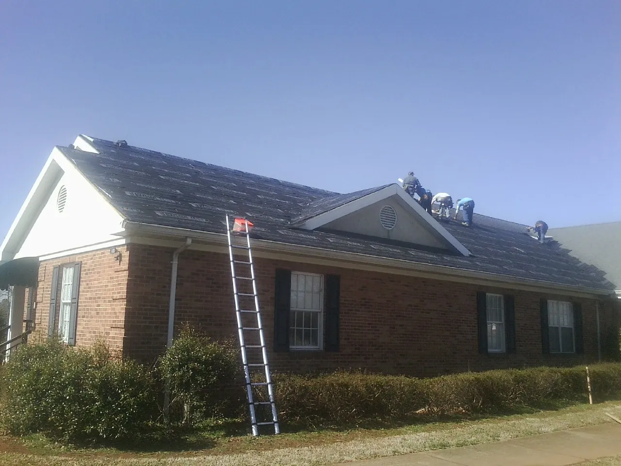 Crew tearing shingles off a brick ranch roof with a ladder set — Metal Roof Repair work by our crew in New Providence